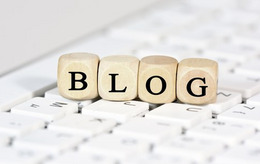 Eine Holzkette mit Buchstaben darauf liegt auf einer Tastatur. Die Buchstaben ergeben das Wort "Blog"