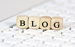 Eine Holzkette mit Buchstaben darauf liegt auf einer Tastatur. Die Buchstaben ergeben das Wort "Blog"