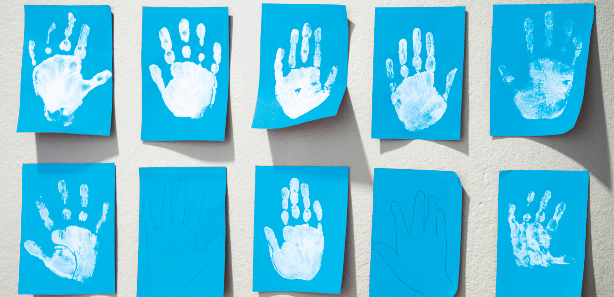 Weiße Abdrücke von Kinderhänden auf blauen Zetteln hängen an der Wand einer Kindertagesstätte. Weiße Abdrücke von Kinderhänden auf blauen Zetteln hängen an der Wand einer Kindertagesstätte.